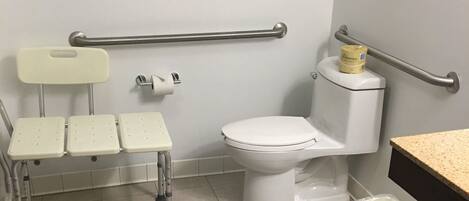 Un bagno con servizi igienici accessibili in sedia a rotelle, maniglione, lavandino e piccolo cestino.