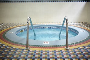A hot tub with two metal ladders, surrounded by a colorful mosaic tile floor.