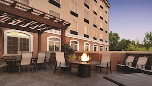 An outdoor patio with a fire pit, seating, and a view of a multi-story building. - Country Inn & Suites by Radisson, Grand Rapids East, MI (Grand Rapids)