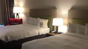 A hotel room with two beds, a red chair, a lamp, and a nightstand with a phone.