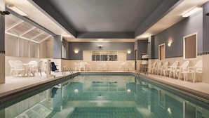 A swimming pool with clear water, surrounded by white chairs and a sunlit area with a glass ceiling. - Country Inn & Suites by Radisson, Grand Rapids East, MI (Grand Rapids)