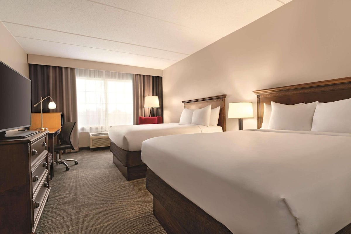 A hotel room with two beds, a desk, a chair, a TV, and a window with curtains.