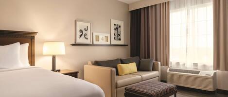 A hotel room with a large bed, a sofa, a small table, and a window with curtains.
