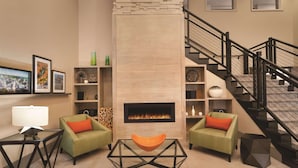 A modern living room with a fireplace, green armchairs, a glass coffee table, and a staircase. - Country Inn & Suites by Radisson, Grand Rapids East, MI (Grand Rapids)