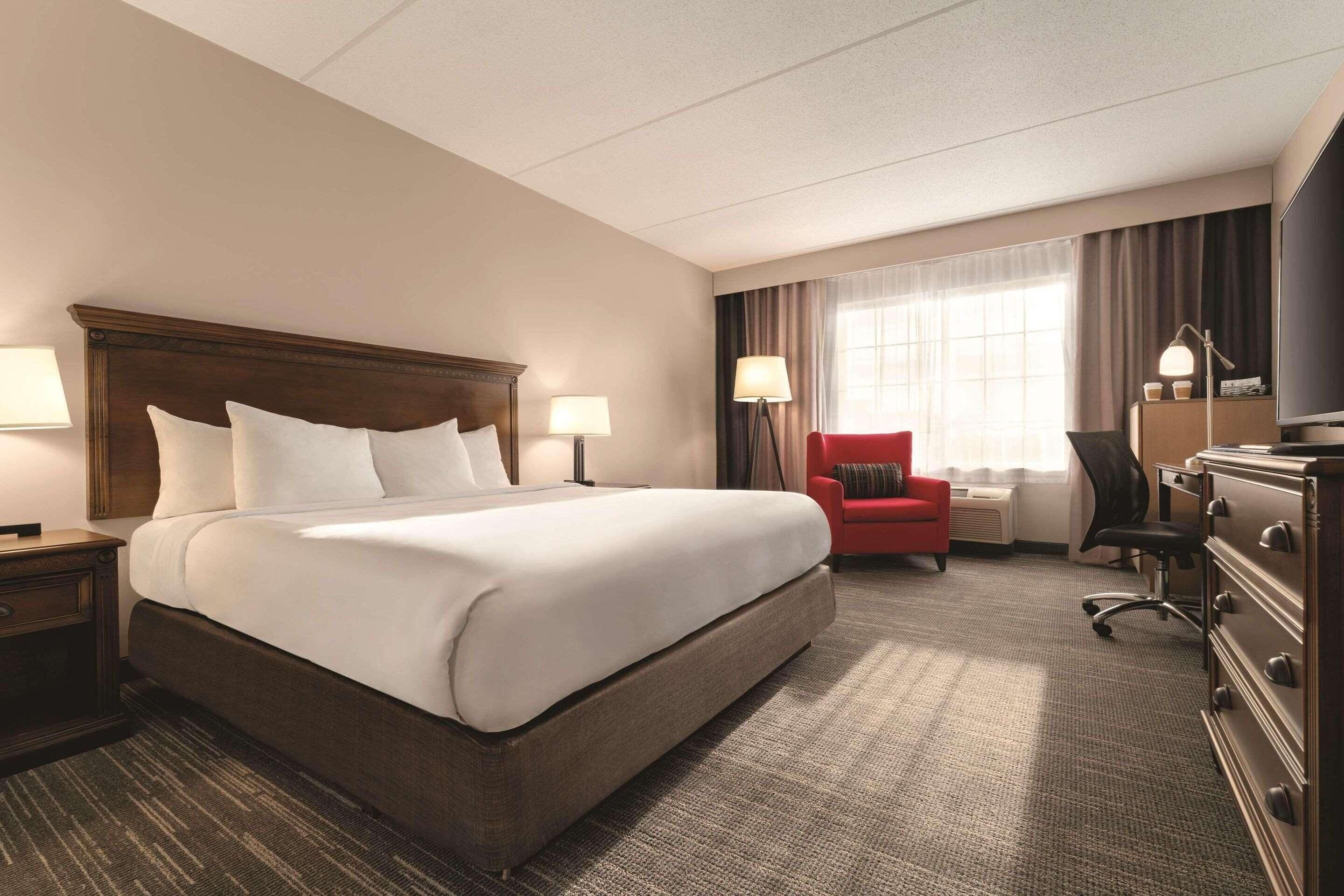 A hotel room with a large bed, a desk, a chair, a dresser, and a television.