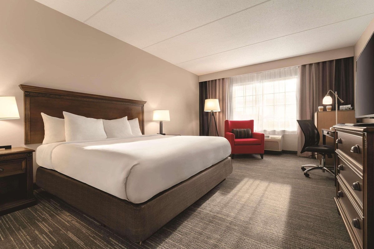 A hotel room with a large bed, a desk, a chair, a dresser, and a television.