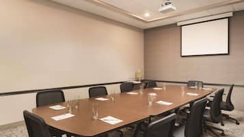Ett konferensrum med ett långt bord, svarta stolar, en projektorduk och ett mattbeklätt golv.