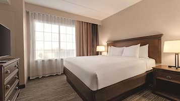 A hotel room with a large bed, two bedside tables with lamps, a TV on a dresser, and a window with curtains.