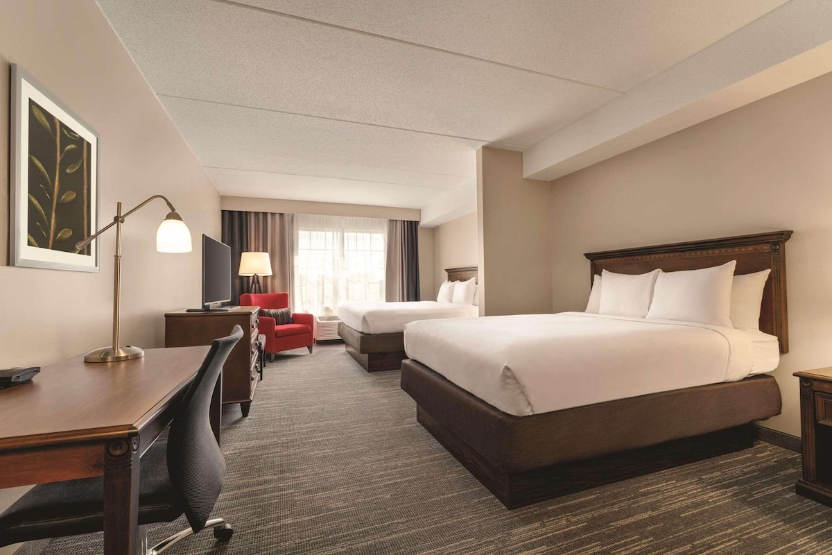 A hotel room with a large bed, a desk, a chair, a TV, and a window with curtains.