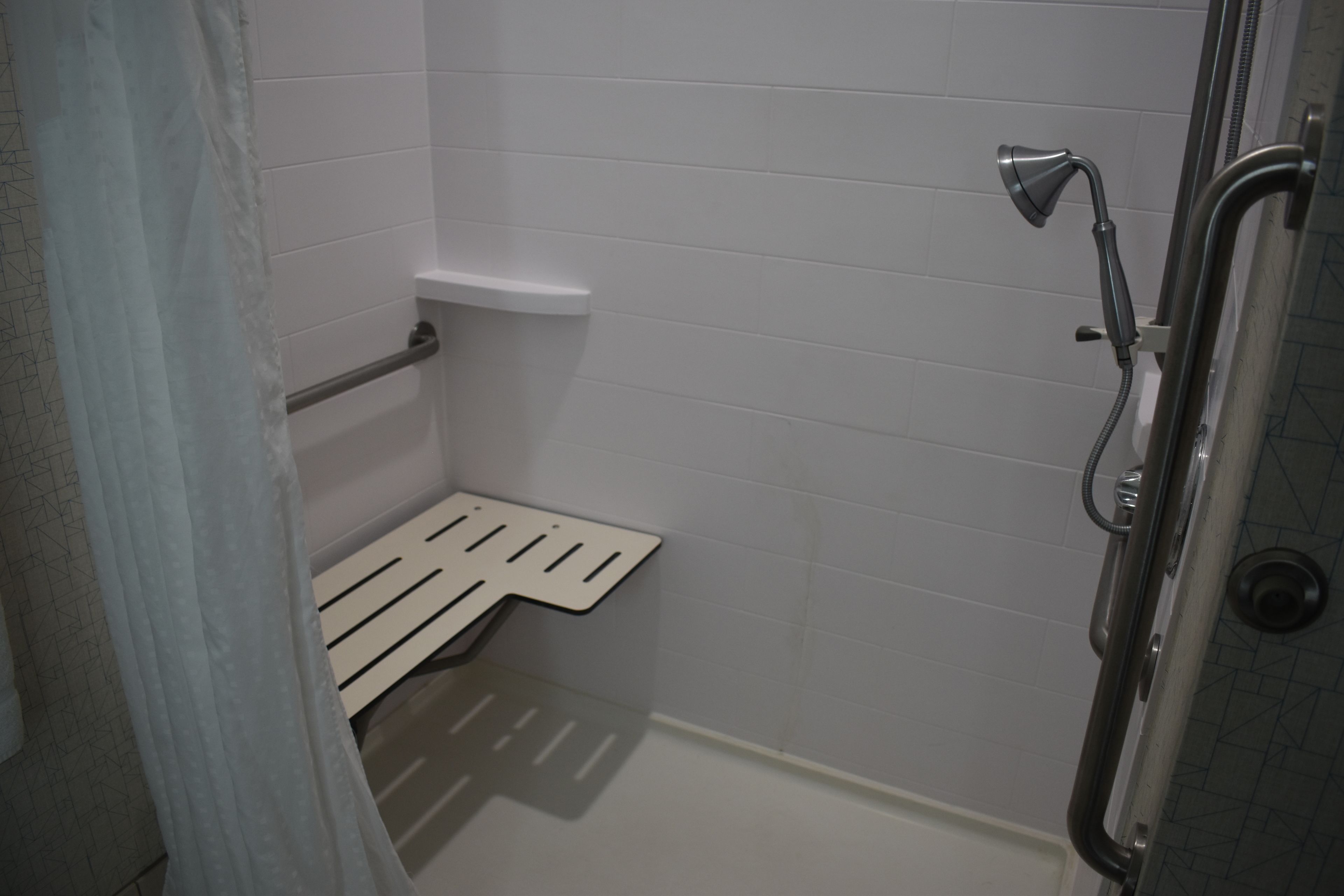 Zona de ducha con barra de apoyo, banco blanco y cabezal de ducha.