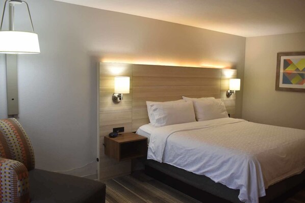 A hotel room with a bed, bedside lamps, a nightstand, and a patterned armchair.