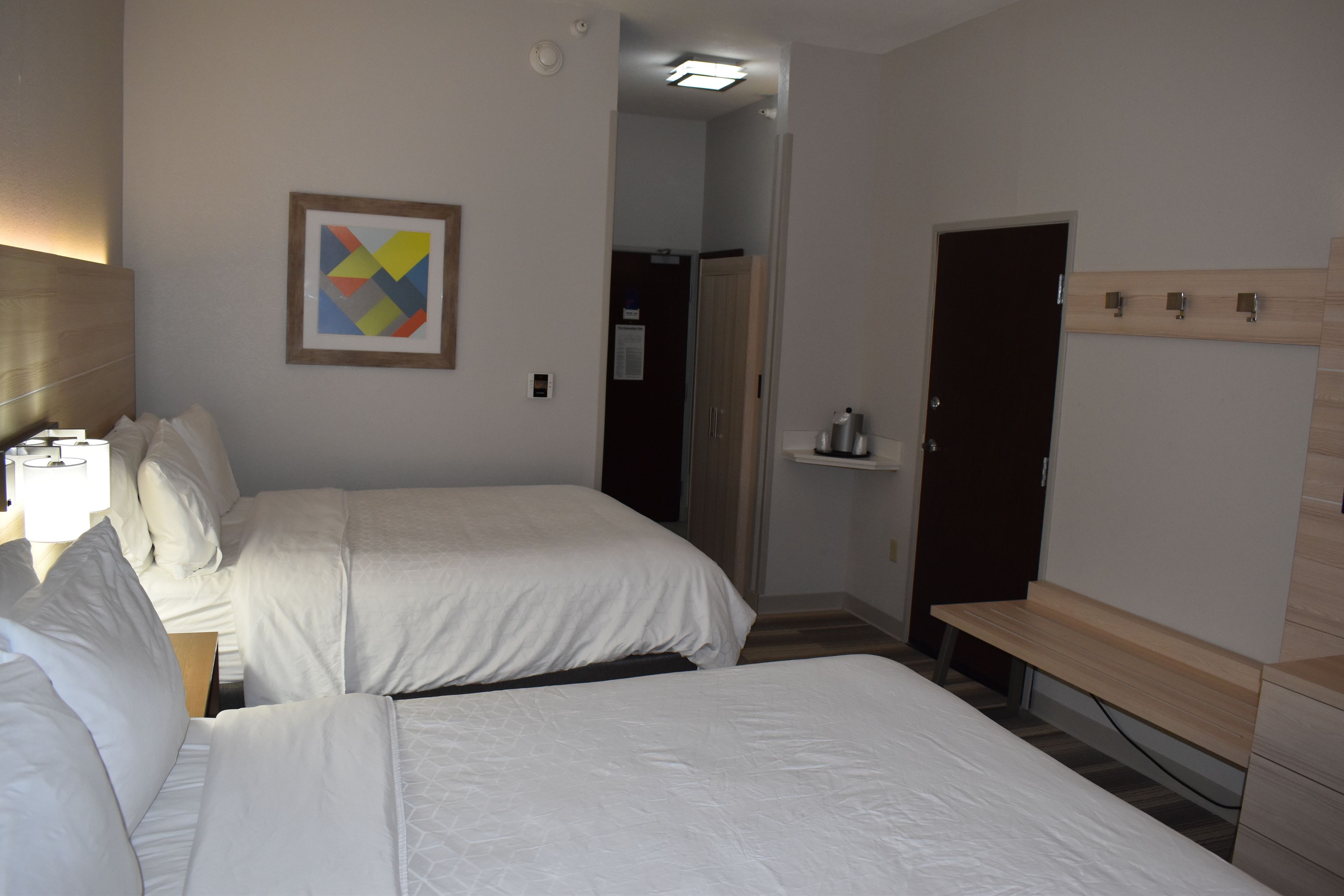 Een hotelkamer met twee bedden, een nachtkastje, een wandplank en een deur naar een badkamer.