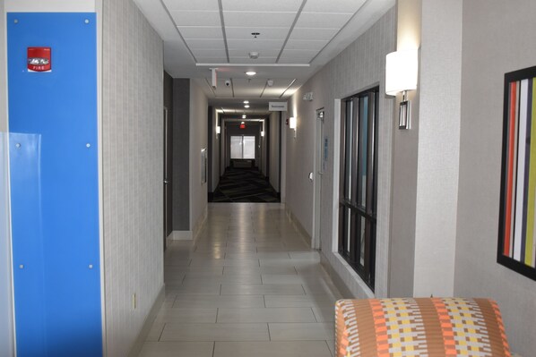 A hotel corridor with a blue elevator, a fire alarm, and a sign for restrooms. - Holiday Inn Express & Suites McPherson by IHG (McPherson)