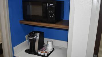 Un coin cuisine avec un micro-ondes noir posé sur une étagère, une machine à café Keurig et plusieurs gobelets jetables.
