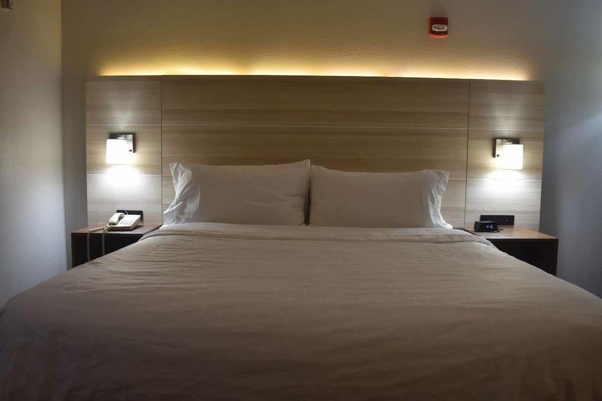 A hotel room with a large bed, two bedside tables, a nightstand, a phone, and a wall-mounted light fixture.