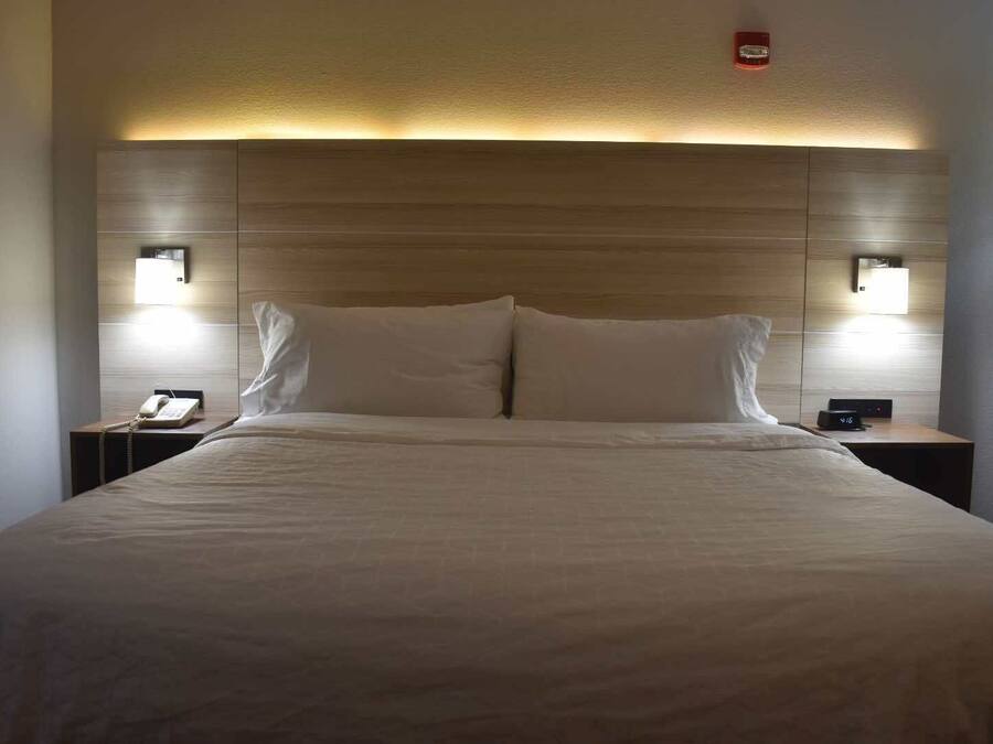 Una habitación de hotel con una cama grande, dos mesitas de noche, un teléfono y una lámpara fijada a la pared.