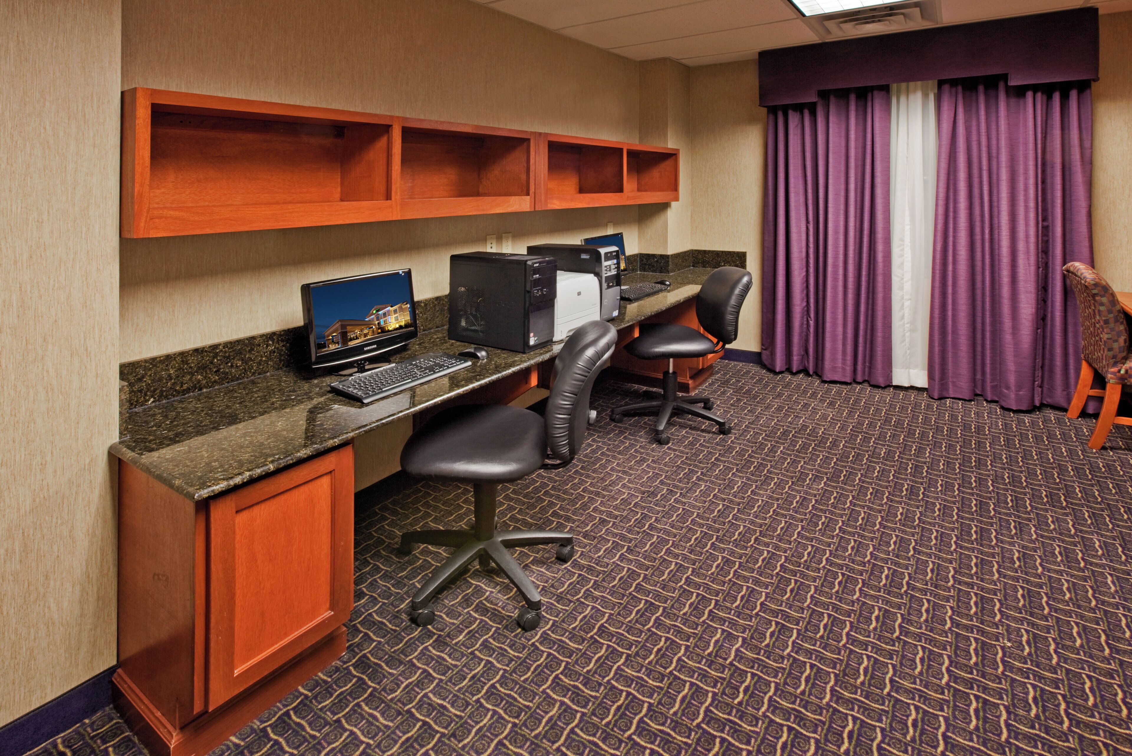 Una habitación de hotel con un escritorio, dos sillas, una computadora y un televisor.