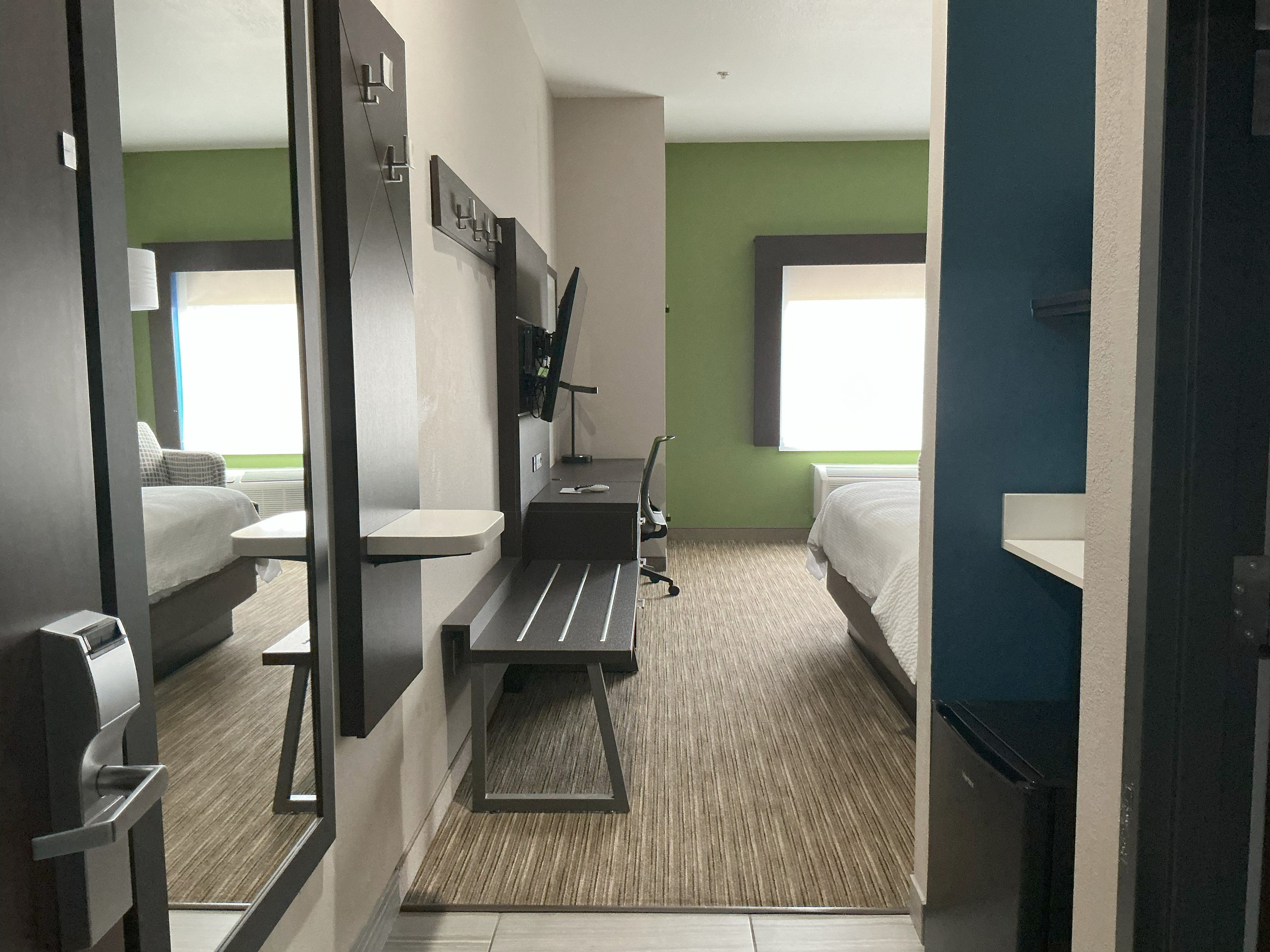 A hotel room with a bed, a desk, a chair, a mirror, and a window.