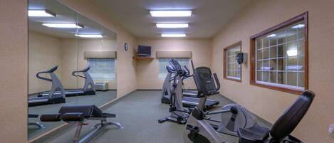 Un gimnasio con equipo de ejercicio, espejos y una televisión.