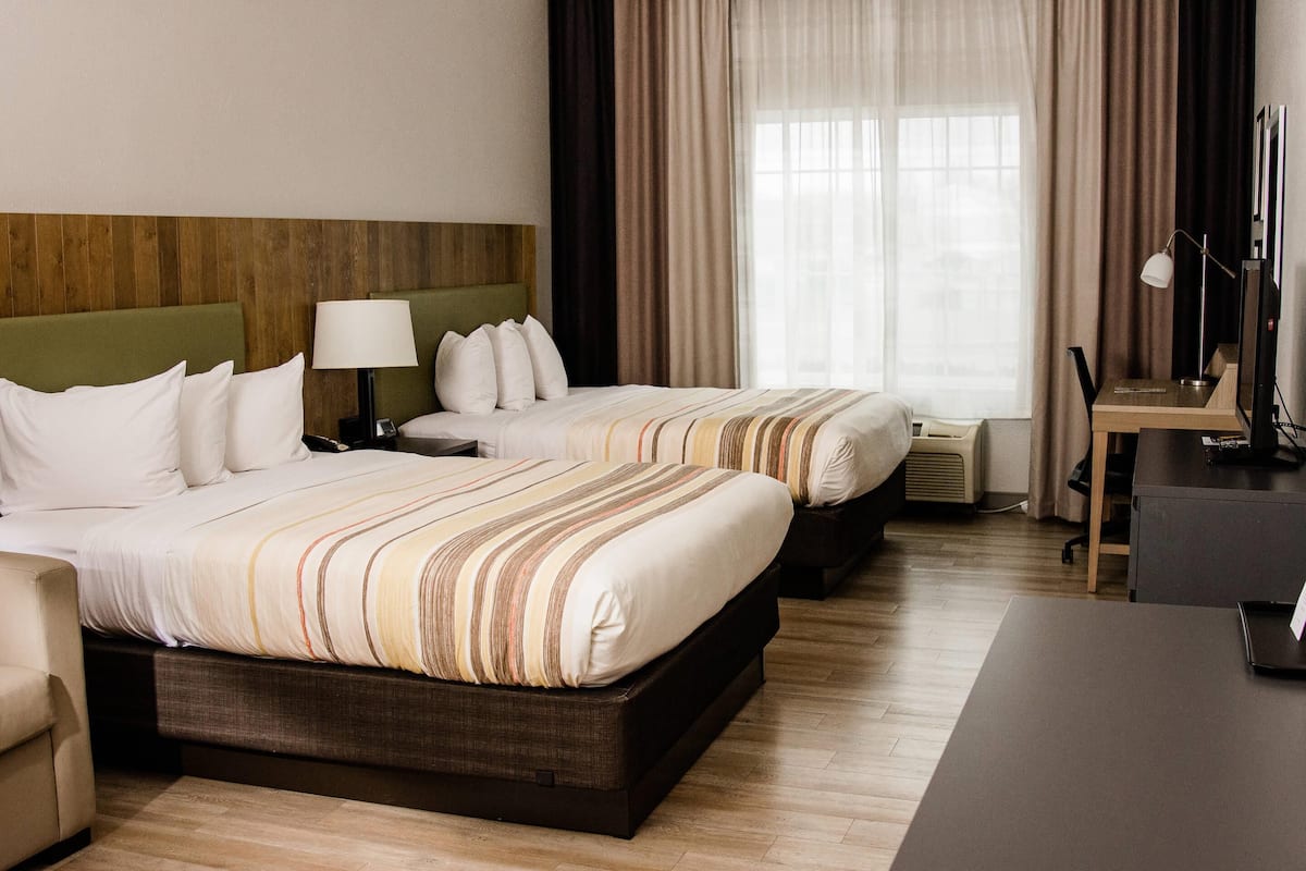A hotel room with two beds, a desk, a chair, a lamp, and a window with curtains.