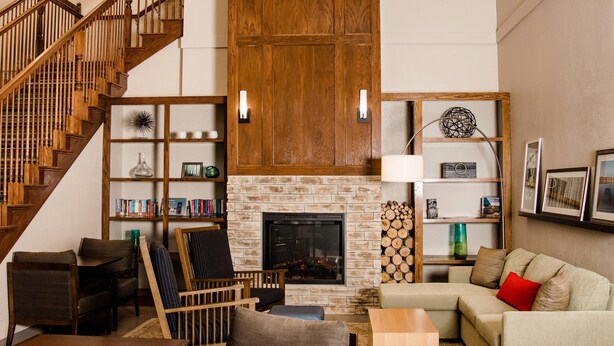 A spacious living room with a fireplace, wooden staircase, and a bookshelf. - Country Inn & Suites by Radisson, Winchester, VA (Winchester)