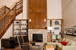 A spacious living room with a fireplace, wooden staircase, and a bookshelf.