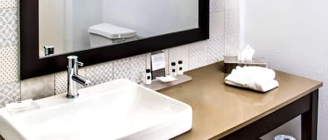 Un baño con un lavamanos grande, un espejo, un perchero para toallas y un inodoro visible en el reflejo.