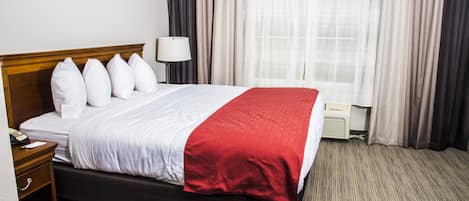 A hotel room with a bed, a bedside table, a lamp, and a window with curtains.
