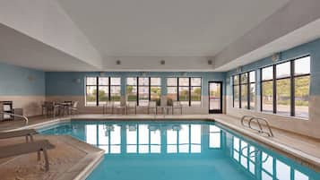 A large indoor swimming pool with clear blue water, surrounded by multiple windows offering views of the outside.