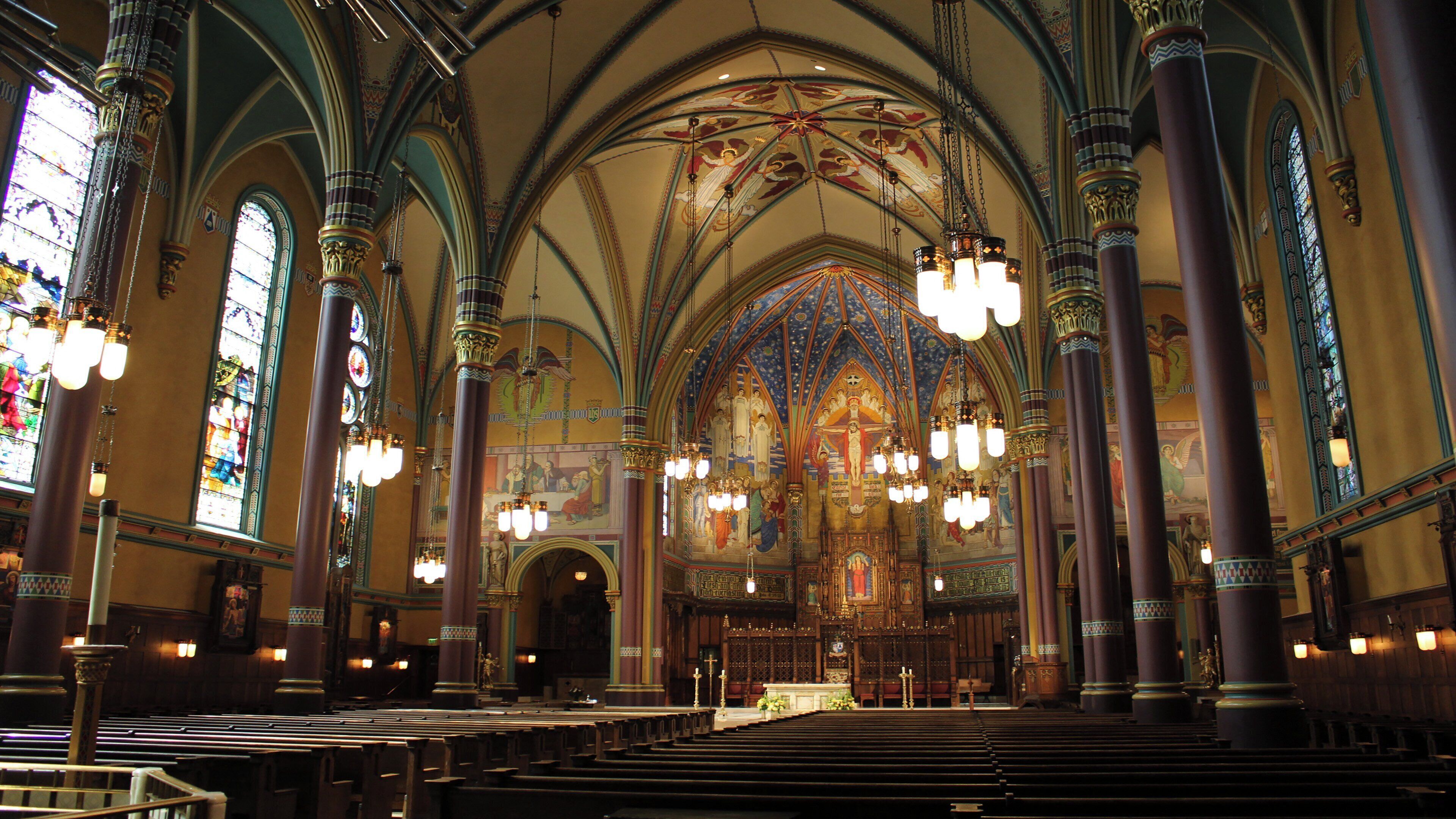 Interior de igreja com altos tetos abobadados, vitrais e colunas ricamente decoradas.