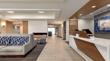 A modern hotel lobby with a reception desk, seating area, and a fireplace.