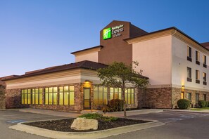 A Holiday Inn Express & Suites hotel with a stone facade, large windows, and a landscaped front yard.