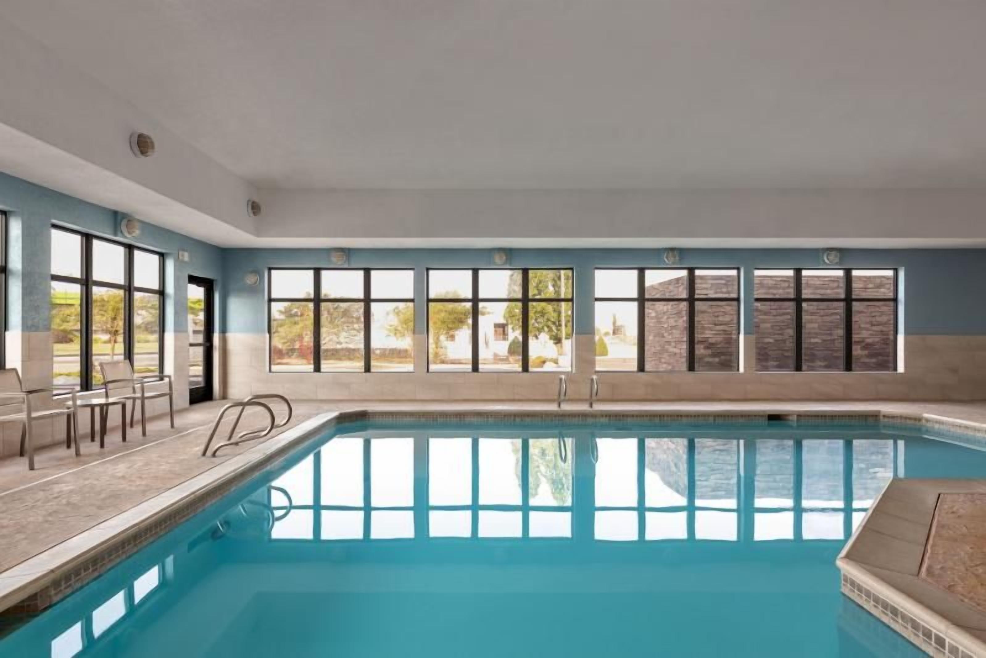 An indoor swimming pool with clear windows, a poolside seating area, and a view of the outside.