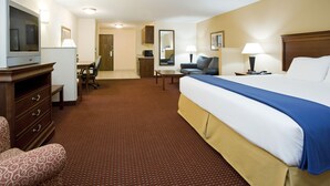 A hotel room with a large bed, a desk, a chair, a television, and a small kitchenette.