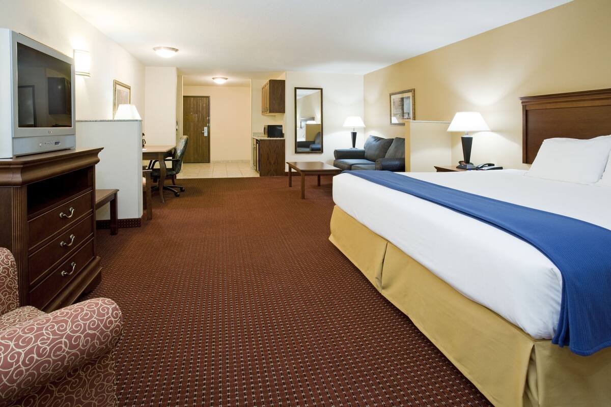A hotel room with a large bed, a desk, a chair, a television, and a small kitchenette.
