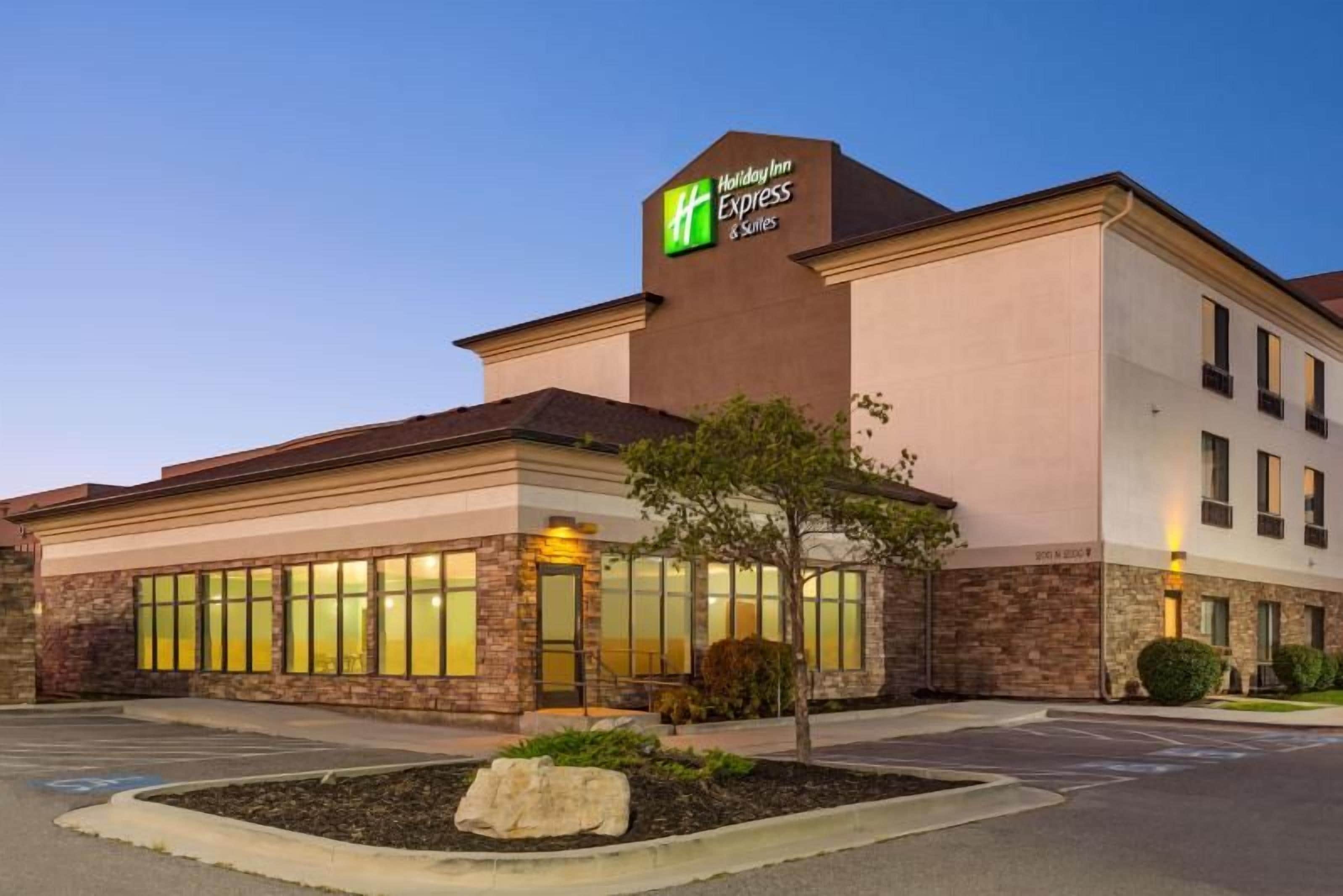 A Holiday Inn Express & Suites building with a brick facade, large windows, and a landscaped front yard.