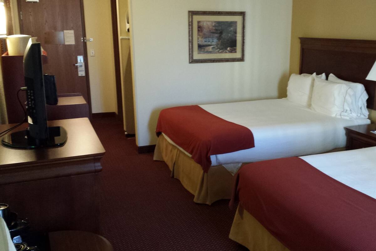 A hotel room with two beds, a TV, a painting on the wall, and a desk with a lamp.