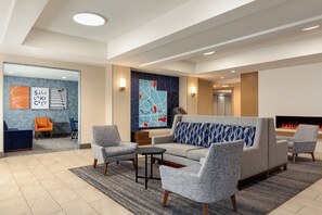 A modern lobby with a sofa, armchairs, a small table, and a fireplace.