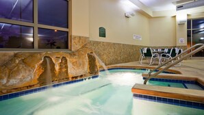 An indoor swimming pool with a stone wall, a seating area with chairs, and a sign indicating no lifeguard on duty. - Holiday Inn Madison at The American Center by IHG (Madison)