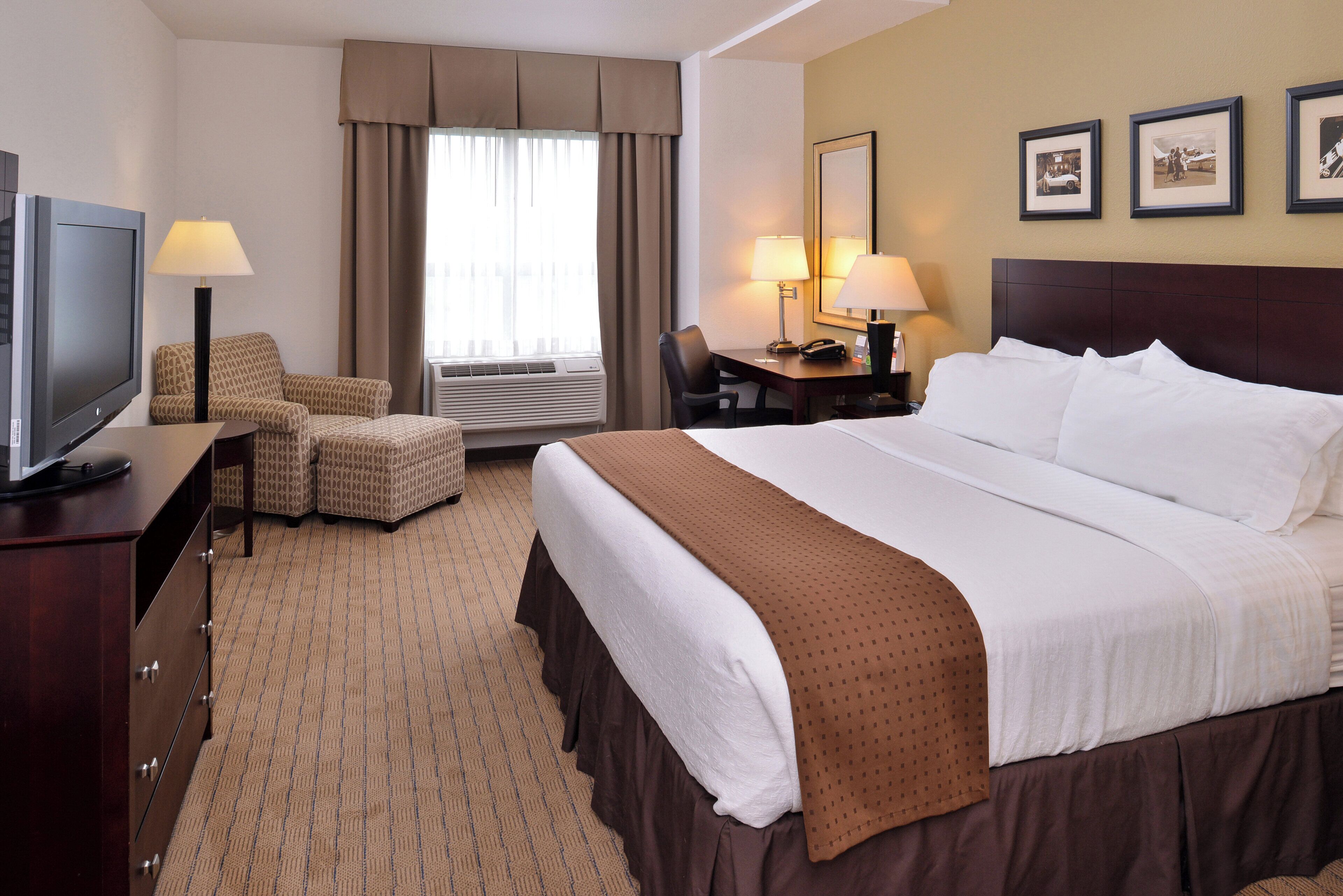 A hotel room with a bed, a desk, a chair, a television, and a window with curtains.