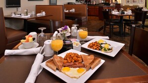 A breakfast setting with two plates of eggs, bacon, and toast, a bowl of fruit, and a glass of orange juice. - Holiday Inn Madison at The American Center by IHG (Madison)