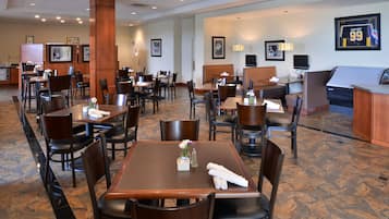 A hotel dining area with multiple tables and chairs, framed pictures on the walls, and a sports jersey on display.