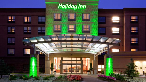 A Holiday Inn hotel with a glass entrance canopy, brick facade, and green lighting. - Holiday Inn Madison at The American Center by IHG (Madison)