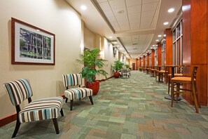 A hotel corridor with striped chairs, potted plants, and a framed picture on the wall. - Holiday Inn Madison at The American Center by IHG (Madison)