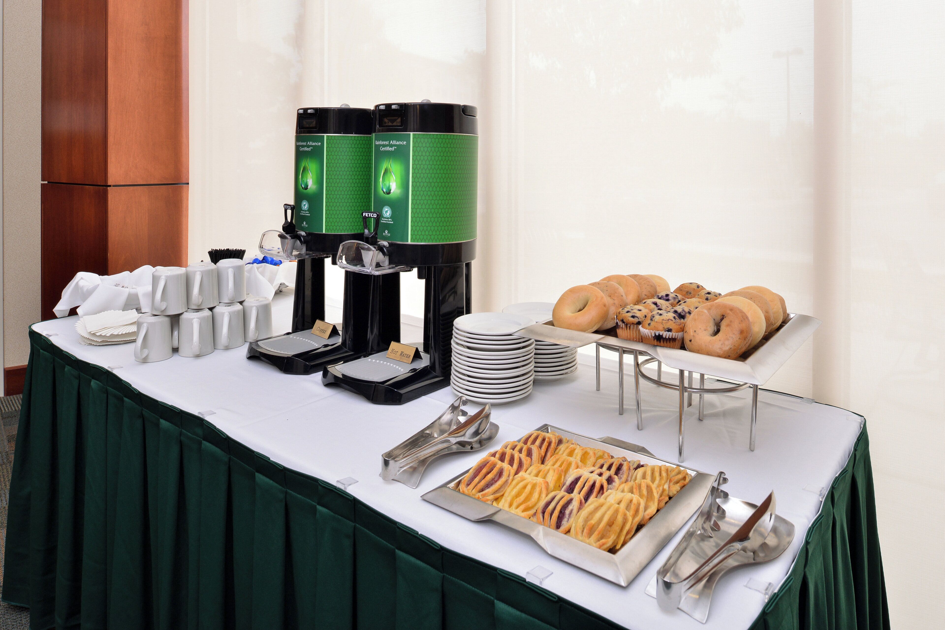 A buffet table with coffee dispensers, plates, bowls, and pastries.