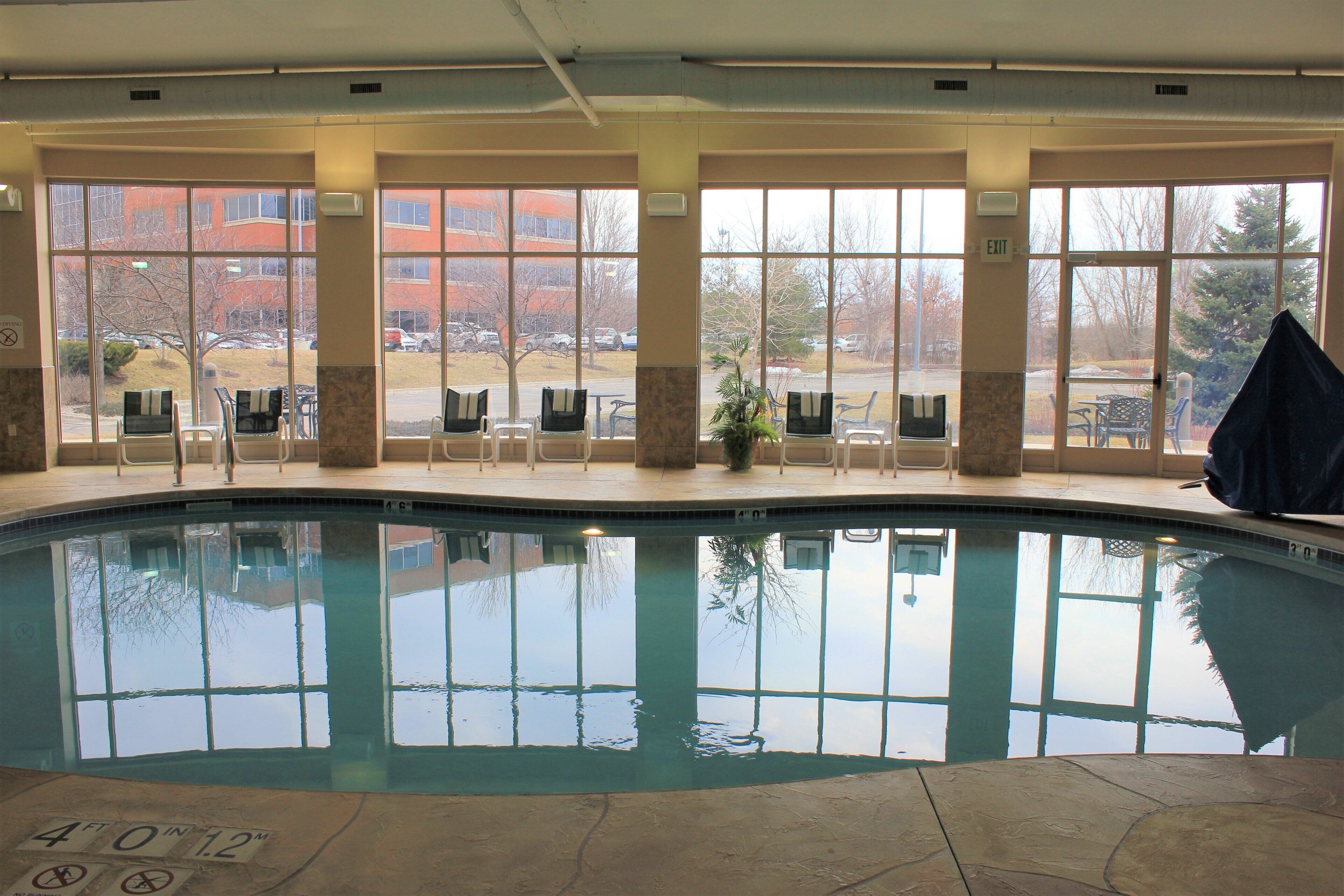 Una piscina interior con paredes de vidrio transparente, suelo de baldosas y vistas a un estacionamiento y edificios.