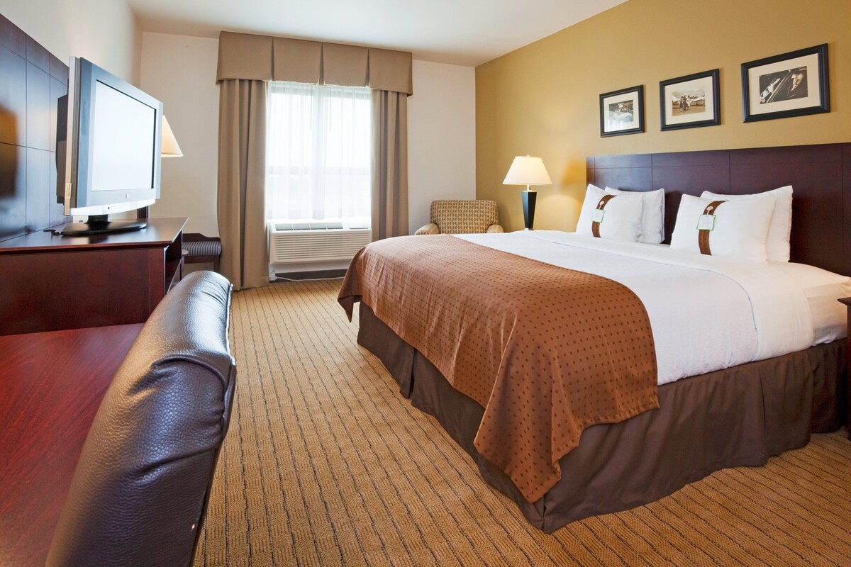 A hotel room with a bed, a desk with a television, a chair, and a window with curtains.