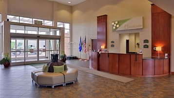 Un hall de hotel con mostrador de recepción, zona de estar y un amplio acceso por puerta de vidrio.