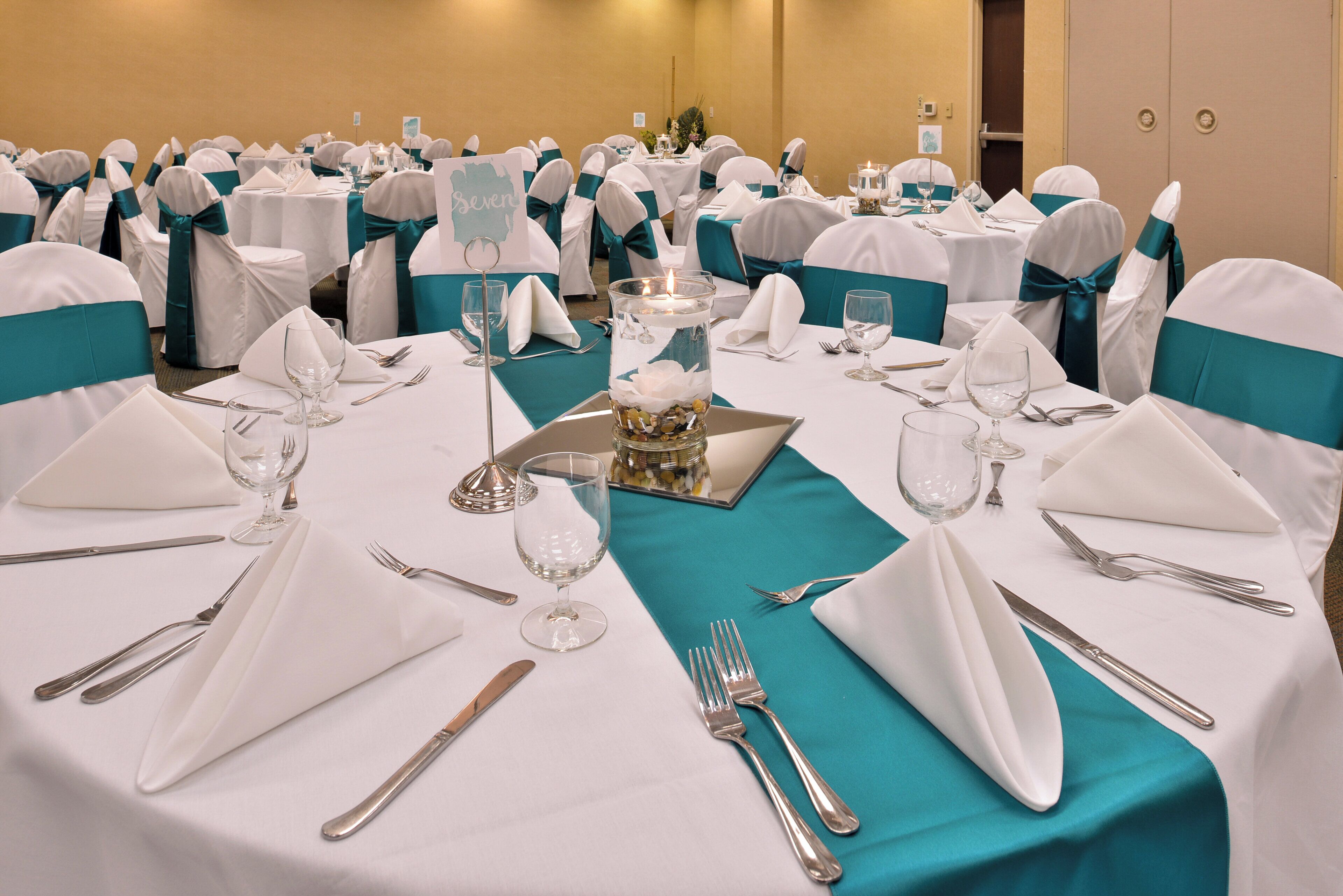 A banquet hall with round tables set for a formal event, complete with white tablecloths, silverware, and glassware.