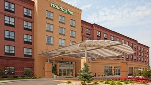 A Holiday Inn hotel with a brick facade, a covered entrance, and a landscaped area with flowers. - Holiday Inn Madison at The American Center by IHG (Madison)